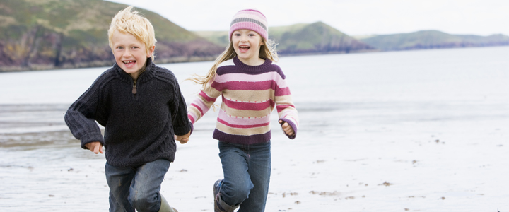 Two young children running on beach holding hands smiling