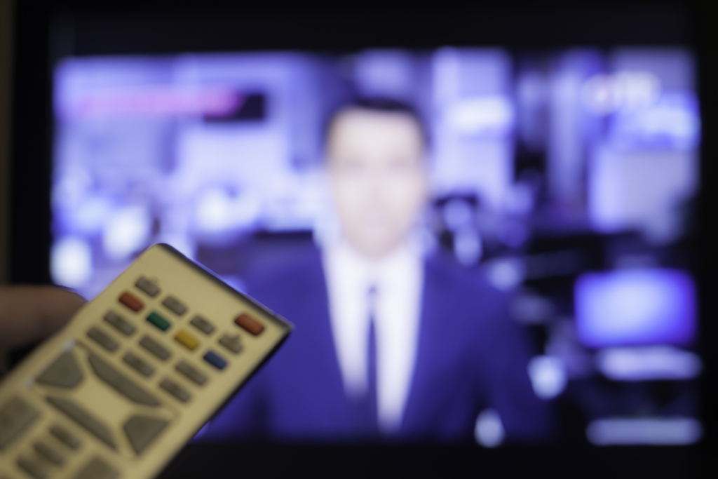 PÅ DIREKTEN. Teksting av direktesendinger er et mangeårig krav fra HLF og står på FNs liste over tiltak for å sikre hørselshemmedes rettigheter. Colourbox Photographer: Yegor Larin Hand holding TV remote with a television in the background