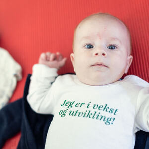 Baby med body med teksten "Vekst og utvikling"