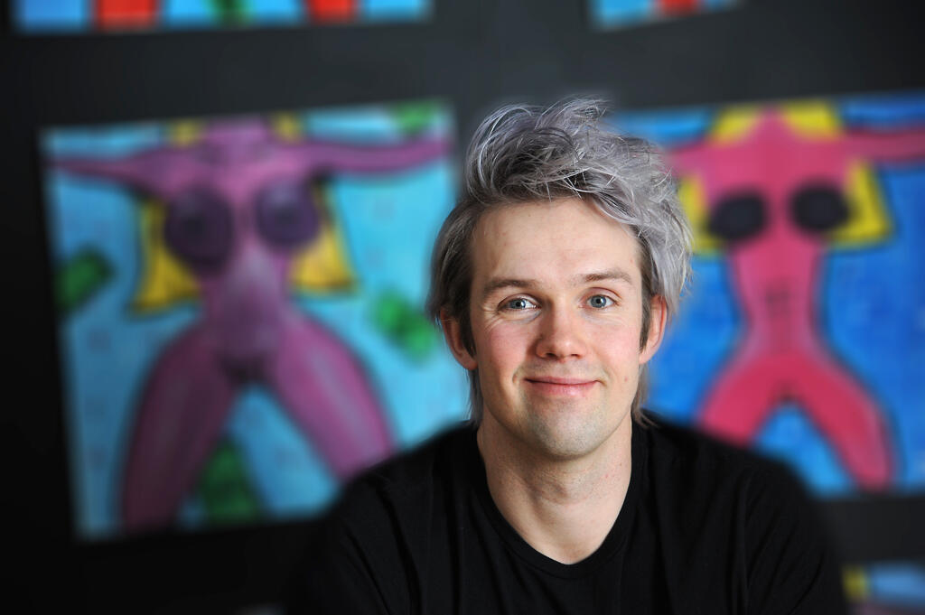 En smilende Nicholas Lund er fotografert foran en fargerik vegg.