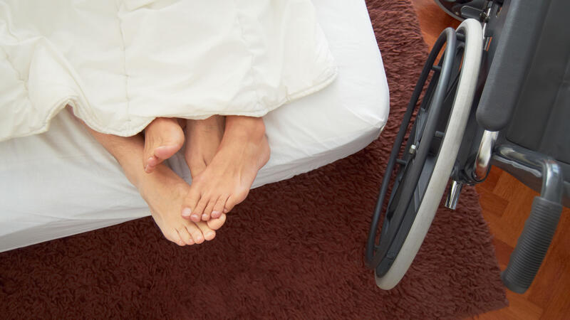 Bilde av to personer under en dyne i en seng, samt en rullestol