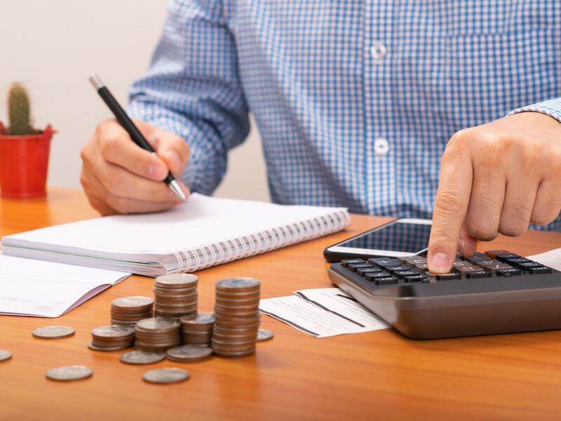 En person arbeider med kalkulator og notatblokk. Mynter er plassert foran personen på bordet