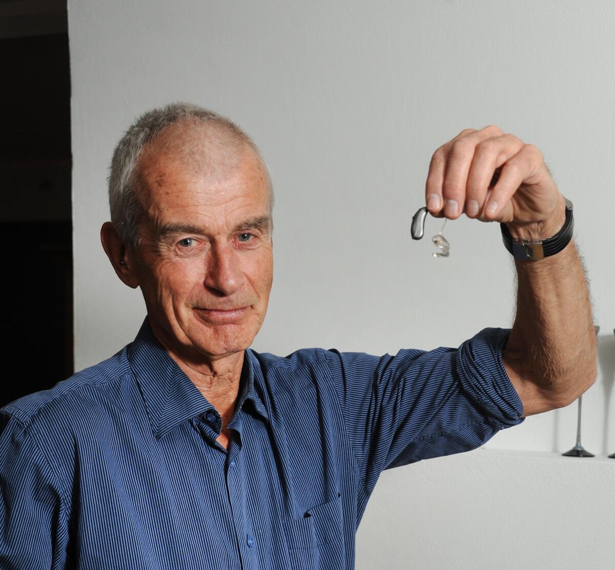 Arne Bakke holder fram det ene høreapparatet sitt.