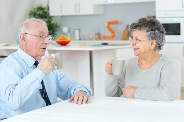 Eldre ektepar sitter ansikt til ansikt og drikker kaffe ved et bord.