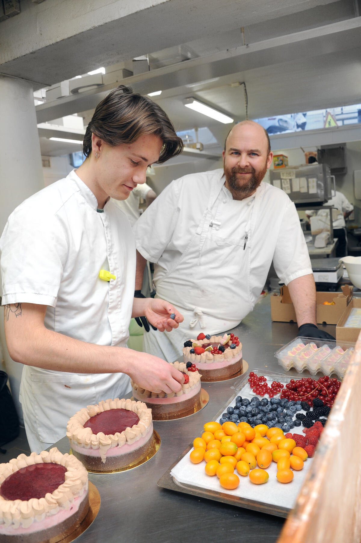 Sjef Morten står ved siden av Kasper som pynter kaker med friske bær