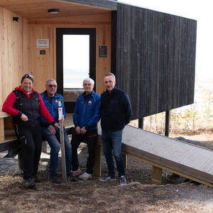 Fire personer som står med en turstolpe utenfor ei hytte