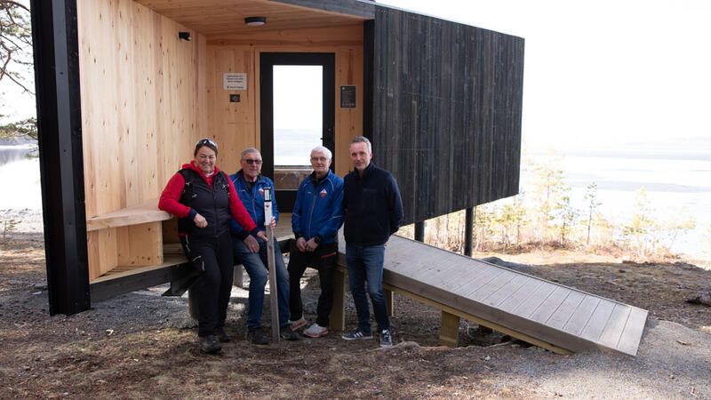 Fire personer som står med en turstolpe utenfor ei hytte