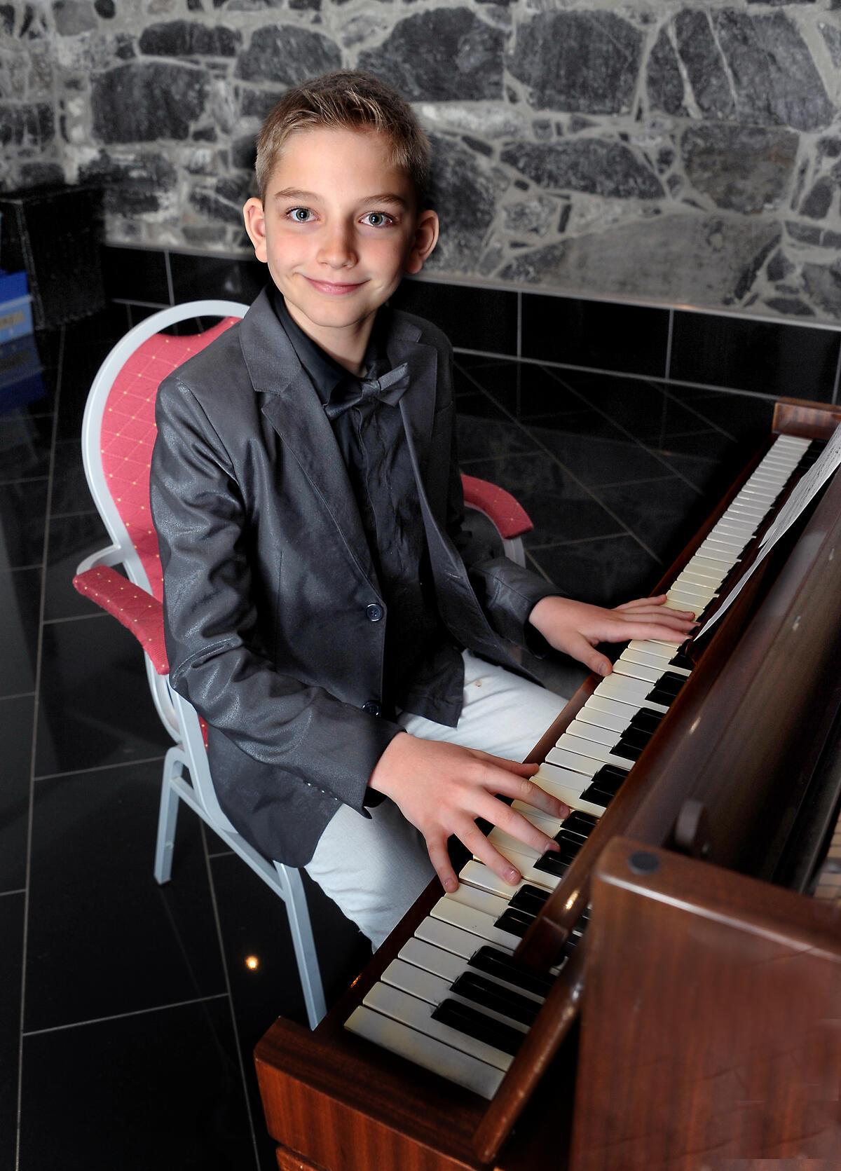 Smilende 11-åring på rød stol spiller piano