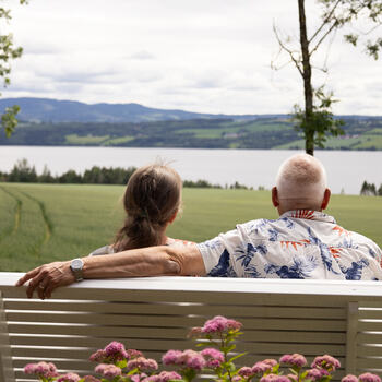 Mann og dame som sitter på en benk og ser ut mot Mjøsa