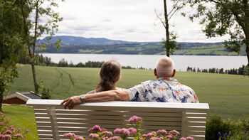Mann og dame som sitter på en benk og ser ut mot Mjøsa