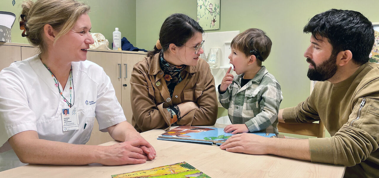 Liten gutt sitter ved et bord sammen med moren, faren og en audopedagog.