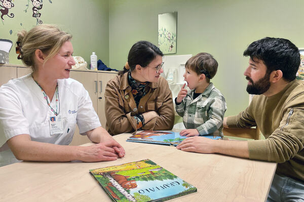 Liten gutt sitter ved et bord sammen med moren, faren og en audopedagog.