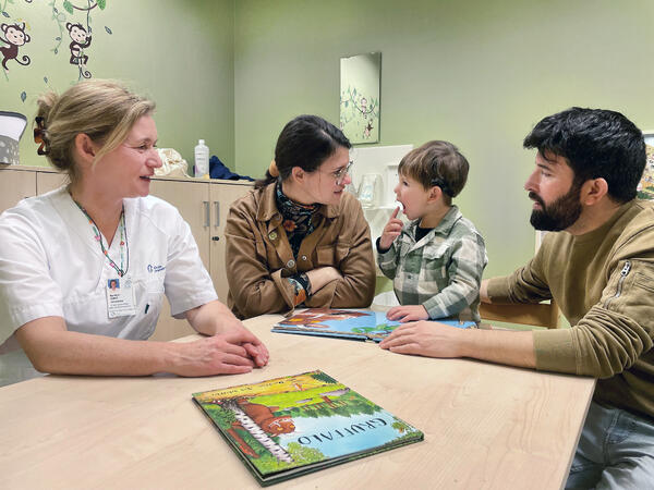 Liten gutt sitter ved et bord sammen med moren, faren og en audopedagog.