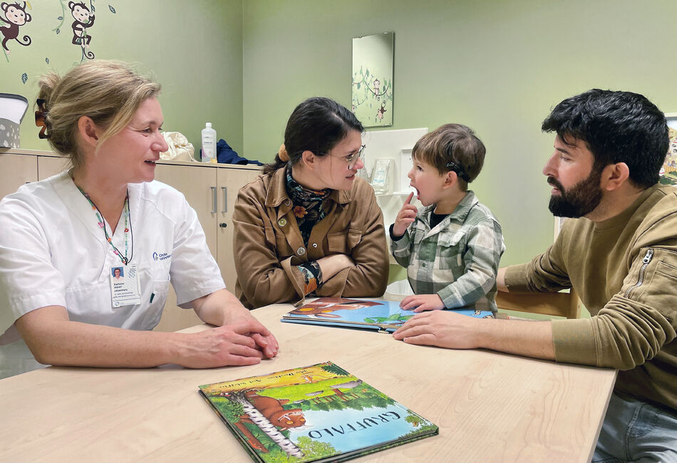 Liten gutt sitter ved et bord sammen med moren, faren og en audopedagog.