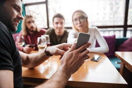 Ung mann viser frem mobilskjerm til venner på en kafé