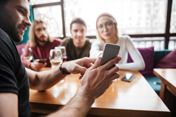 Ung mann viser frem mobilskjerm til venner på en kafé