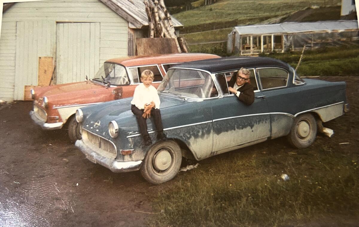 Ung gutt stikker hodet utav bilvindu på en gammel blå Opel. Liten guutt sitter på panseret