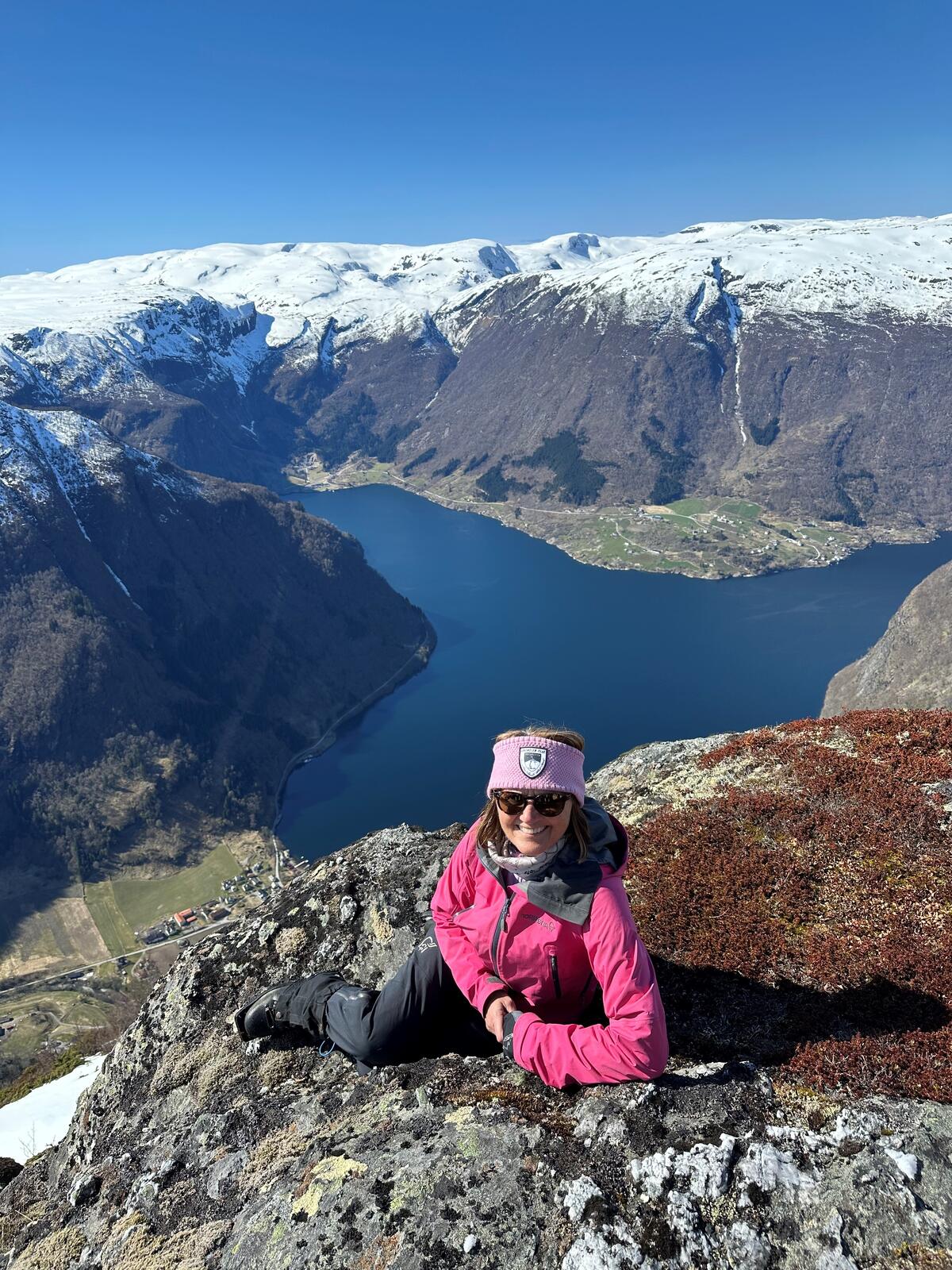 Bilde av dame i rosa turjakke på høyt fjell med Sognefjorden i bakgrunnen