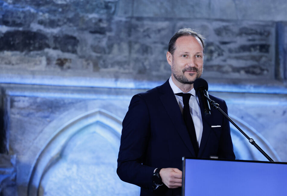 Kronprins Haakon i svart dress foran en talestol