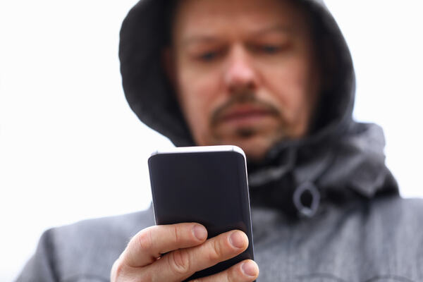 Bilde av mann med regnhette som ser på mobilskjermen sin
