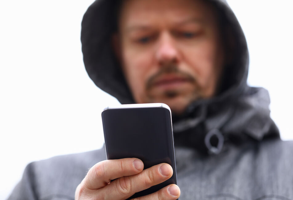 Bilde av mann med regnhette som ser på mobilskjermen sin