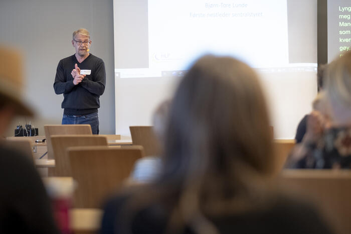Mann i mørk genser holder foredrag og gestiklurere