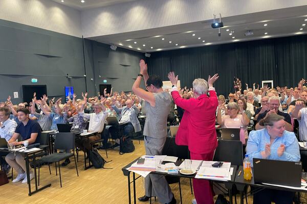 To damer snur seg mot forsamlingen med hendene i været