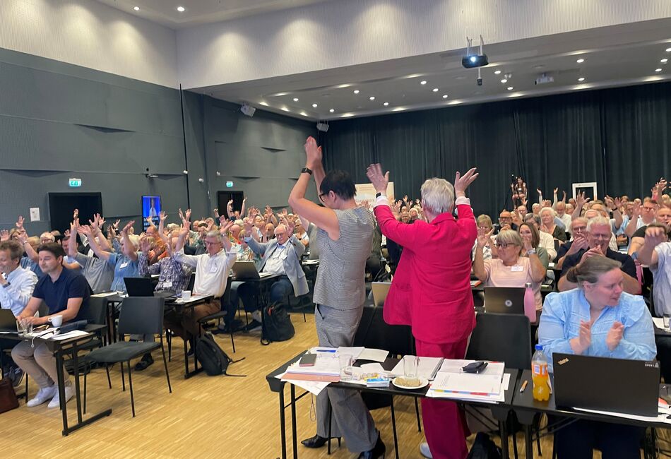 To damer snur seg mot forsamlingen med hendene i været