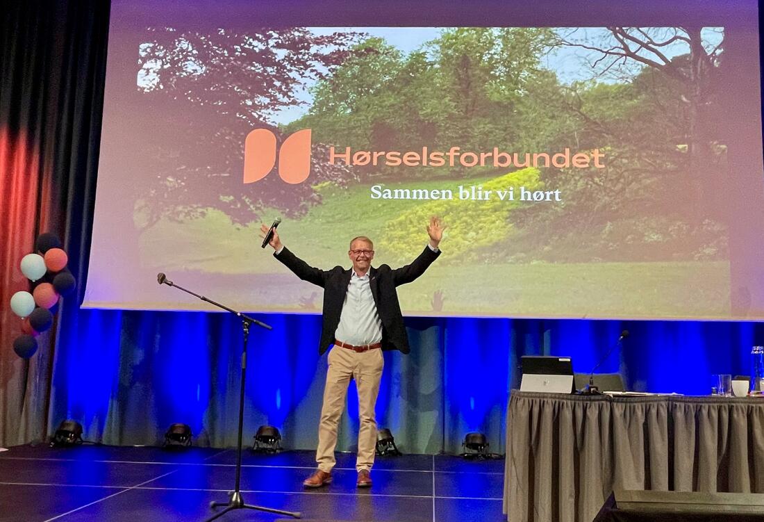 Mann på scenen med løftet hender