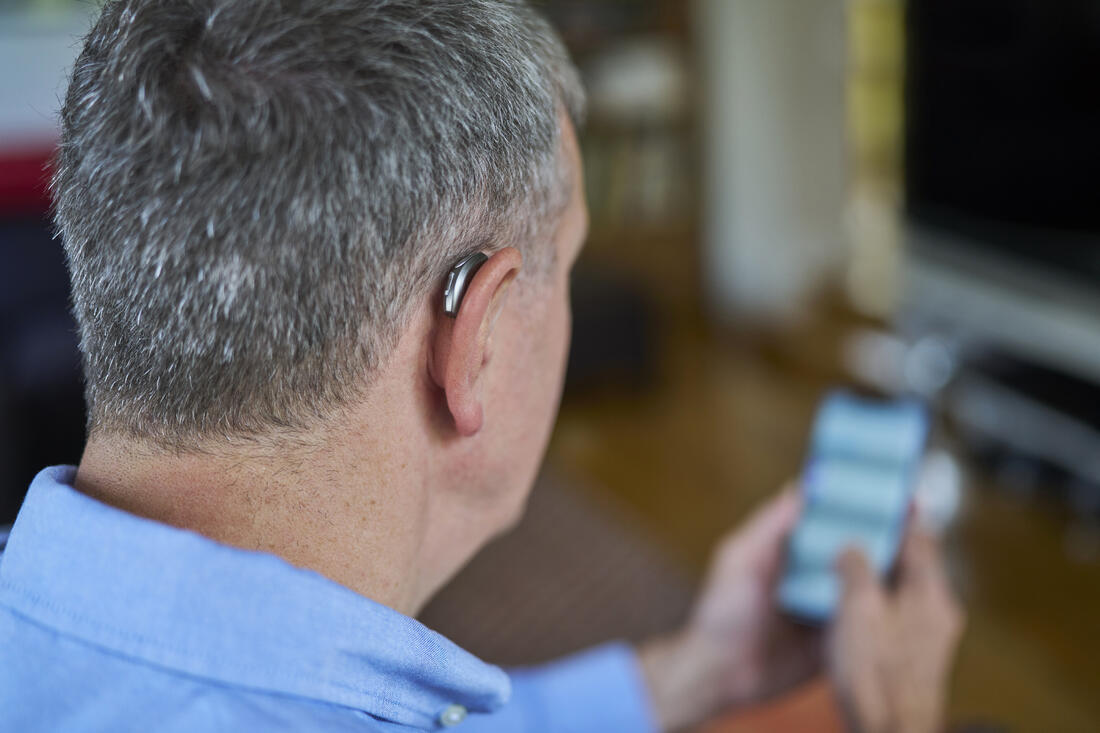 Mann med høreapparat bruker mobilapp for å styre lyden