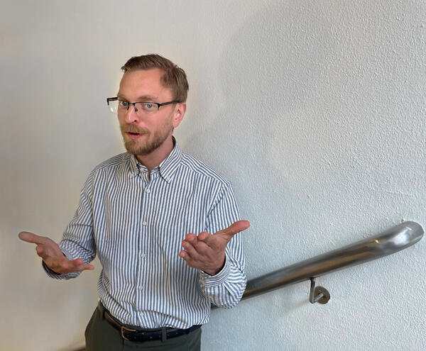 Han ved hvit vegg som gestikulerer med hendene