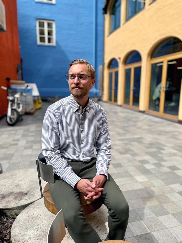Mann sitter på en steinmur i en bakgård og ser til side
