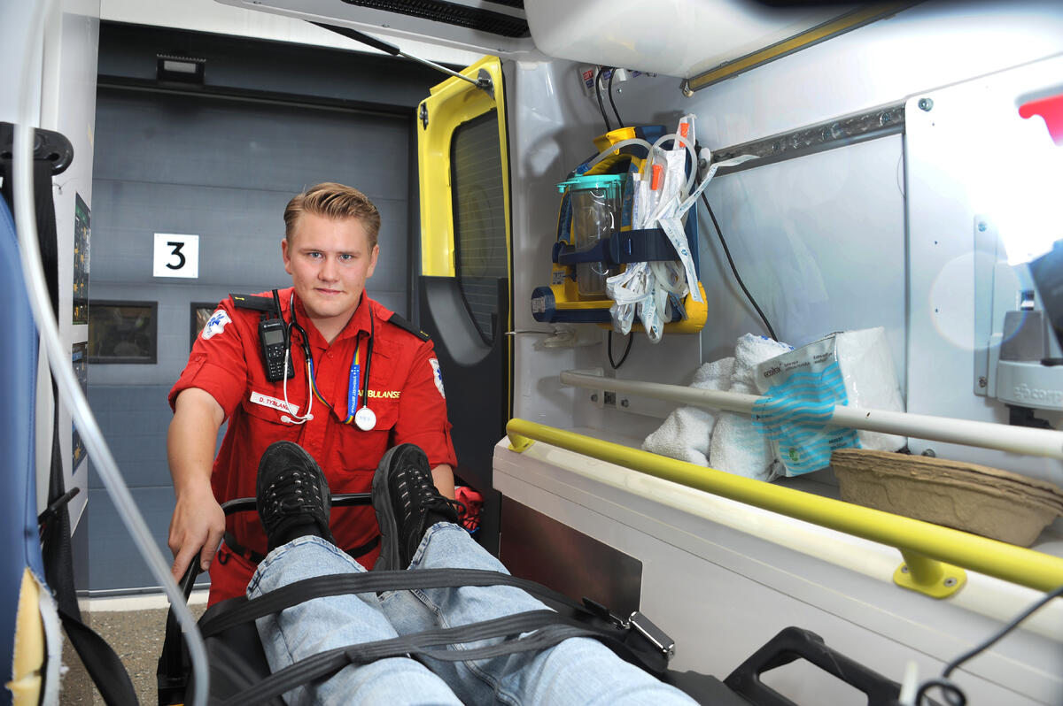 HØRSELEN ER VIKTIG. Det kan være vanskelig å høre hva pasienter med svak stemme sier. For Daniel blir den non-verbale kommunikasjonen ekstra viktig. Mann i ambulanseuniform legger en pasient inn i sykebil