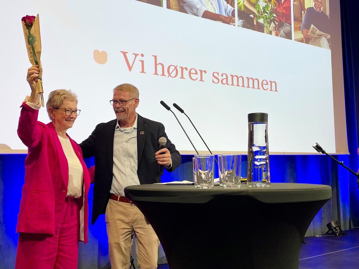 Dame i rosa løfter en rose i hånda og mannen ved siden av smiler