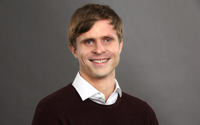 MANUELT. NRK vil fortsette å direktetekste ved hjelp av mennesker, opplyser tilgjengelighetssjef Kristoffer Lium inntil teknologien blir bedre. Foto: NRK Ole Kaland Mann med mørkt hår og vinrød genser