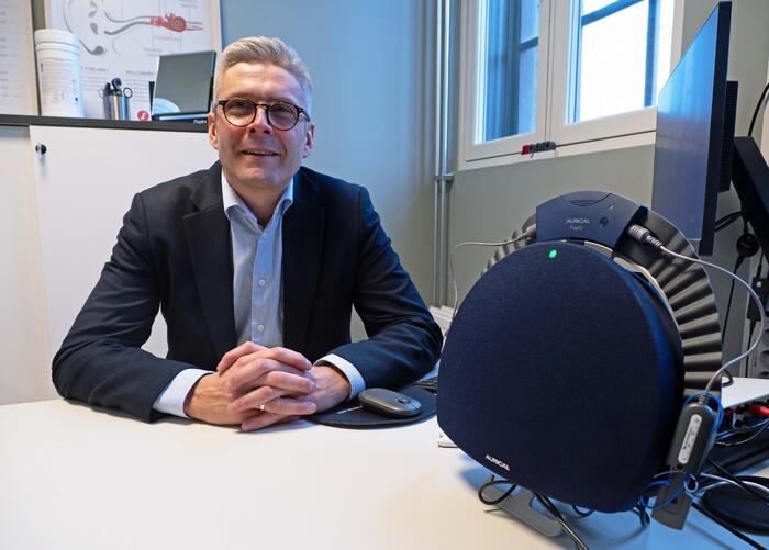MÅNEDSVIS: Marius Collin-Tiller har regnet på nødladere og konstaterer at de holder høreapparatene med strøm i flere måneder. Foto: Georg Mathisen Marius Collin-Tiller bak skrivebord med testutstyr.