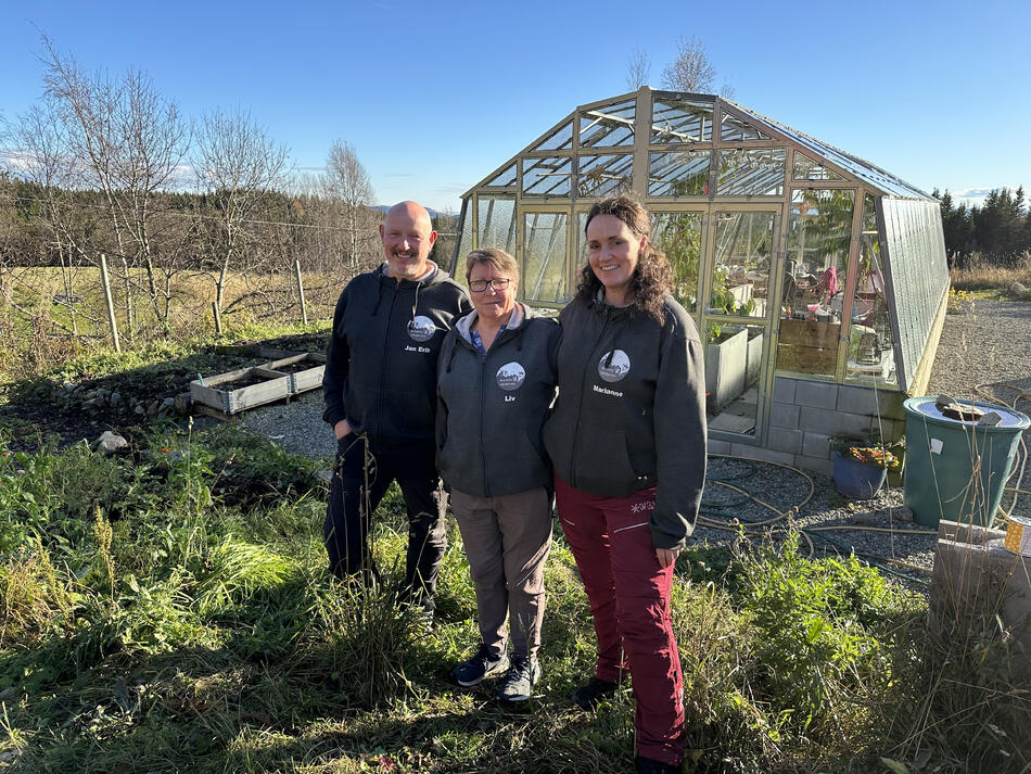 Mann og to damer foran et drivhus