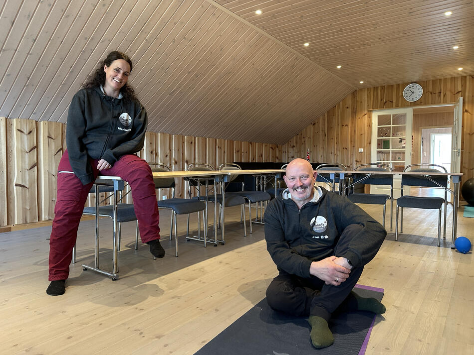 Dame og mann inne på et kursrom. Dama sitter på bordet, mannen på gulvet.