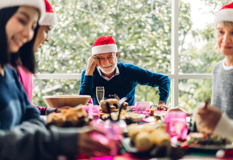 Eldre mann med nisselue sitter rundt et bord med andre gjester med nisselue