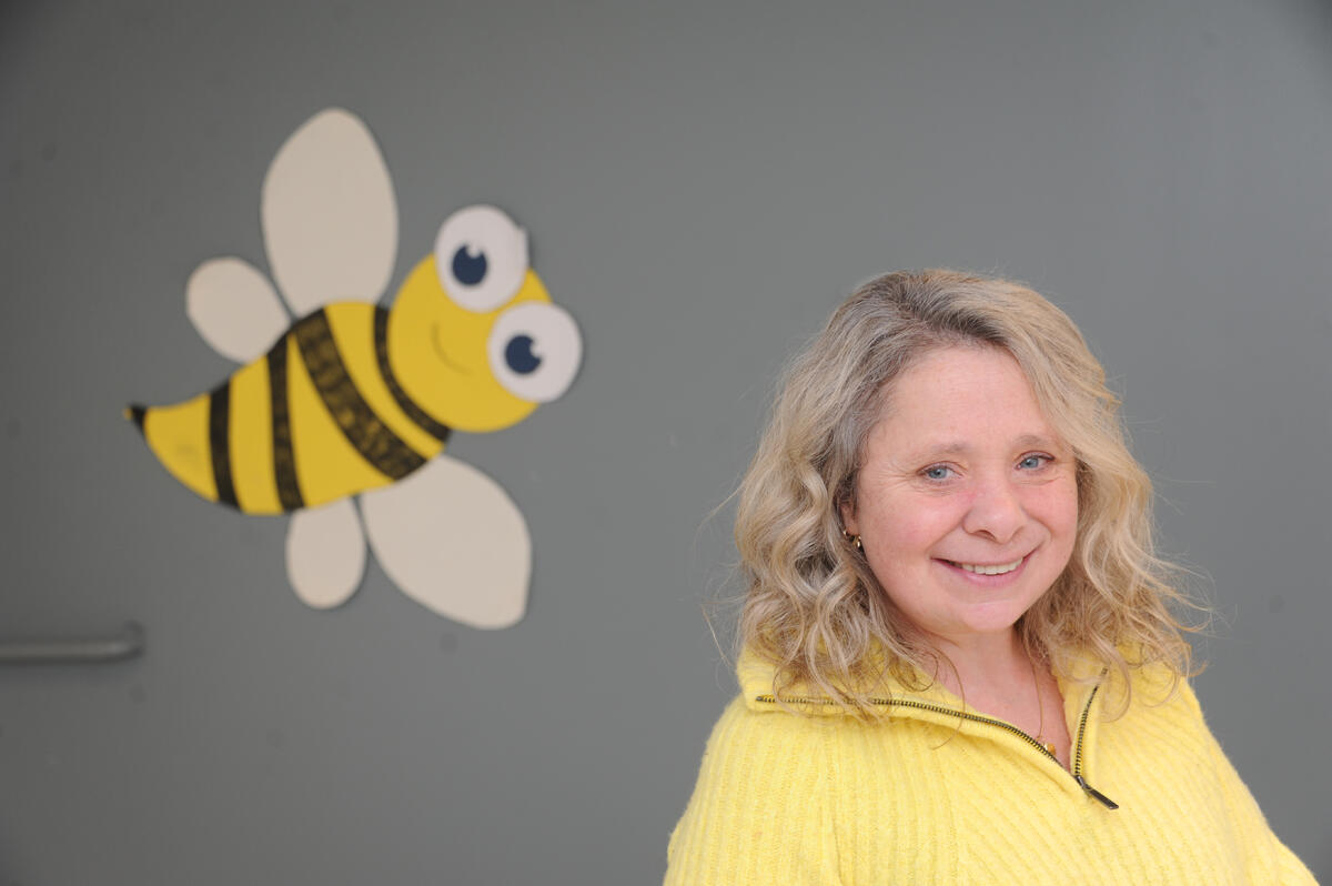 ET GODT LIV. Eli Steinum har valgt å bruke egne erfaringer til å hjelpe fremtidens voksne. Det gjør hverdagen god og meningsfull. Dame i gul genser smiler foran en gul bie