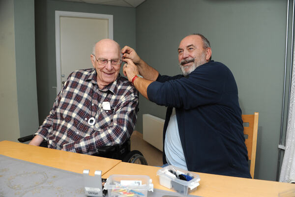 GLAD FOR HJELP. 87 år gamle Oddbjørn er en av beboerne som får sjekket høreapparatene når likeperson John Sandvik har «kontortid» på Edwin Ruuds omsorgssenter. Mann hjelper eldre mann med å sette høreapparat i øret