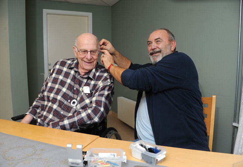 Mann hjelper eldre mann med å sette høreapparat i øret