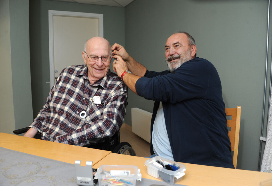 Mann hjelper eldre mann med å sette høreapparat i øret