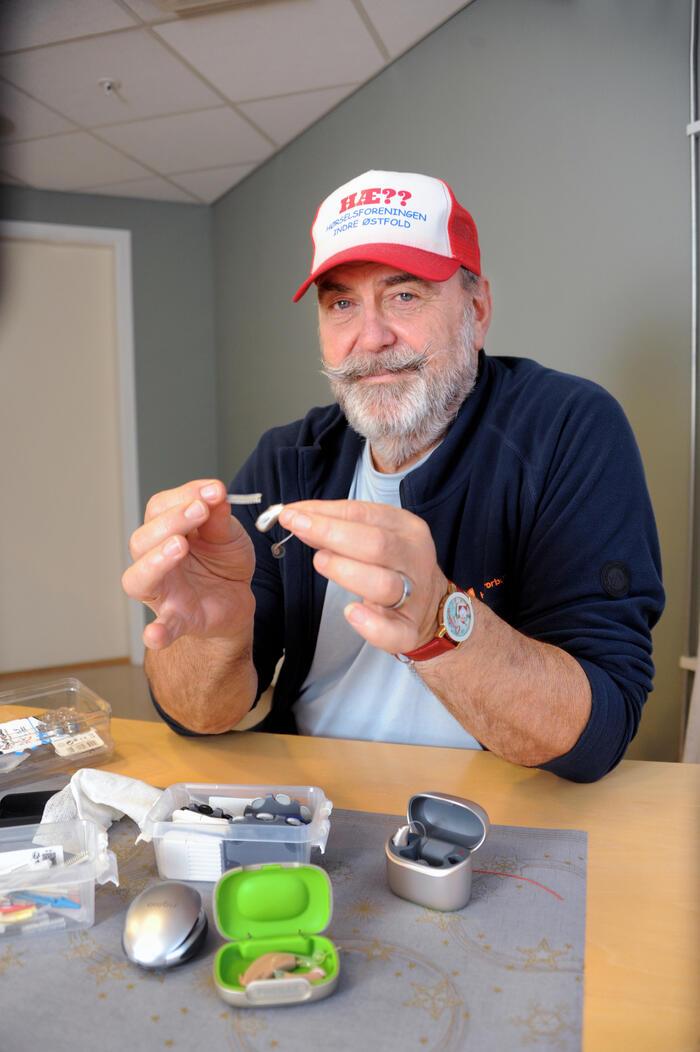 Mann med caps renser et høreapparat