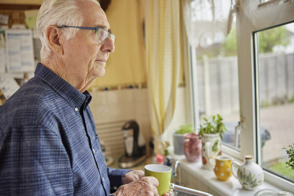 Eldre mann ser ut av et vindu med grønn kaffekopp i hendene