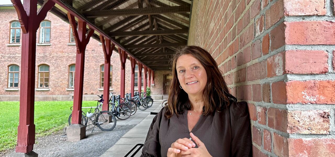 Dame står lent inntil en rødbrun murvegg