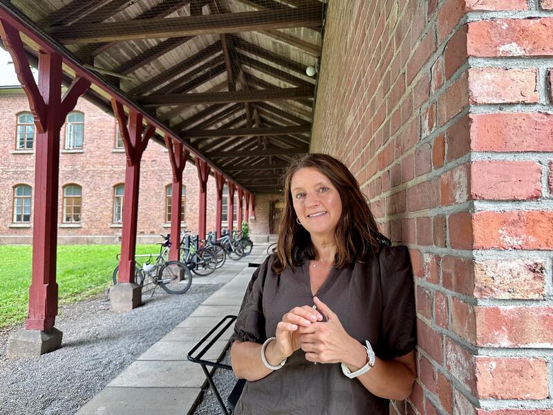 Dame står lent inntil en rødbrun murvegg